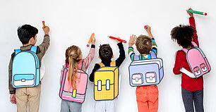 Enfants avec cartable de dos qui dessinent sur un mur