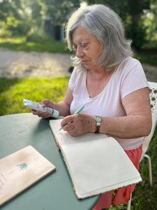 Dame qui lit les ingrédients sur un tube assise à une table dans un jardin.
